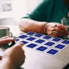 Bliskie ujęcie dłoni dwóch osób rozkładających duże karty mindalo na stole. To wizualizacja prostej gry dla seniorów, wspierającej ćwiczenie pamięci w swobodnej atmosferze.